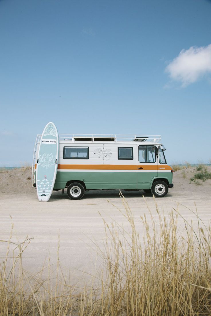 an old van with a surfboard on the roof parked in front of some tall grass