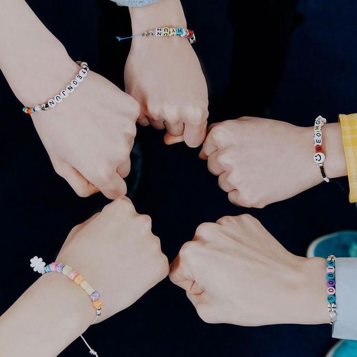 four people holding hands in the middle of a circle with bracelets on their wrists