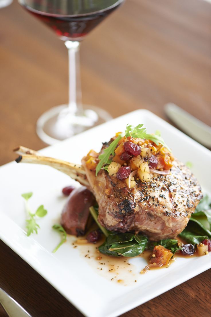 a white plate topped with meat and veggies next to a glass of wine