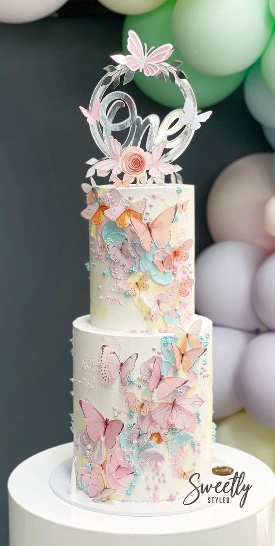 a three tiered cake with butterflies on top and the number one on it's side