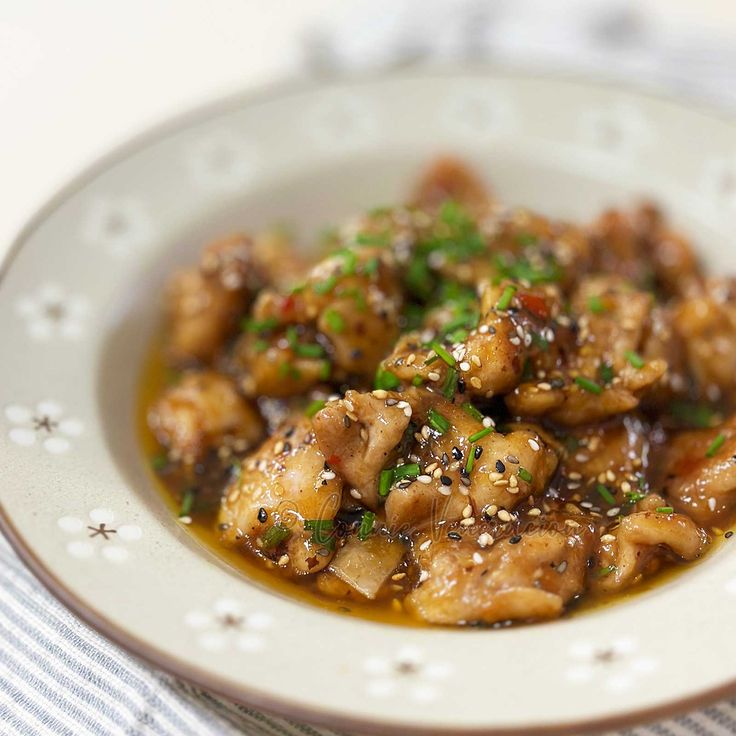 a white plate topped with meat covered in sauce and garnished with sesame seeds