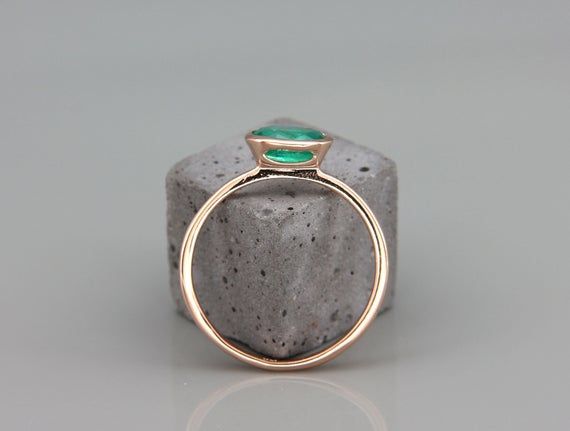 a gold ring with a green stone in the middle on top of a gray rock