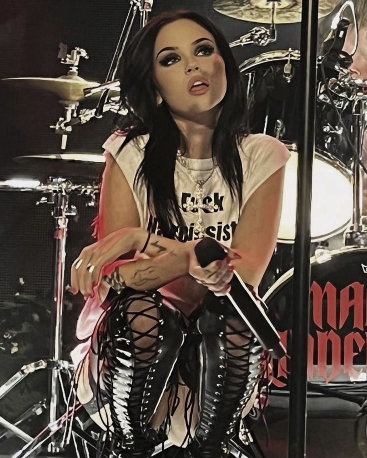 a woman sitting on top of a stage next to a drum set and microphone in her hand