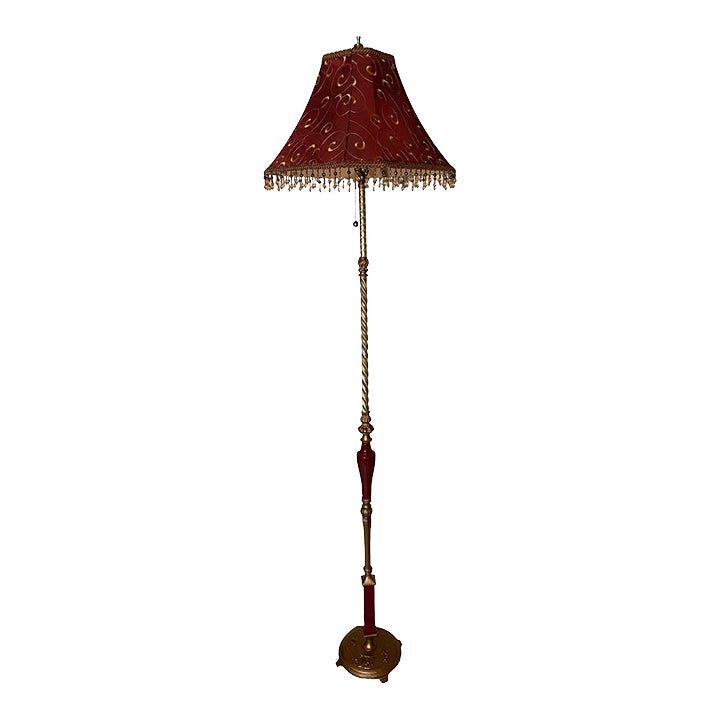 a floor lamp with a red shade on the top and chain hanging from it's side