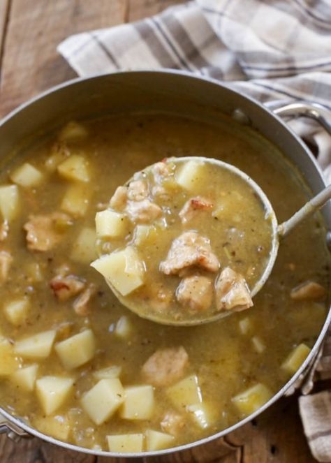 a ladle full of soup with meat and potatoes in it on a wooden table