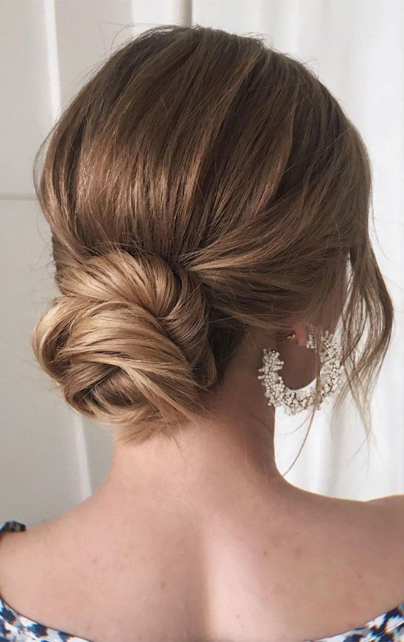 a woman with her hair in a low bun, wearing earrings and a floral dress