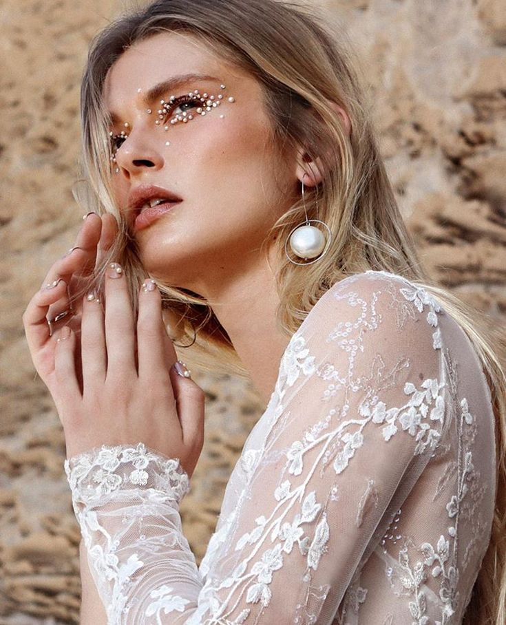 a woman with gold glitter on her face and hands, posing in front of rocks