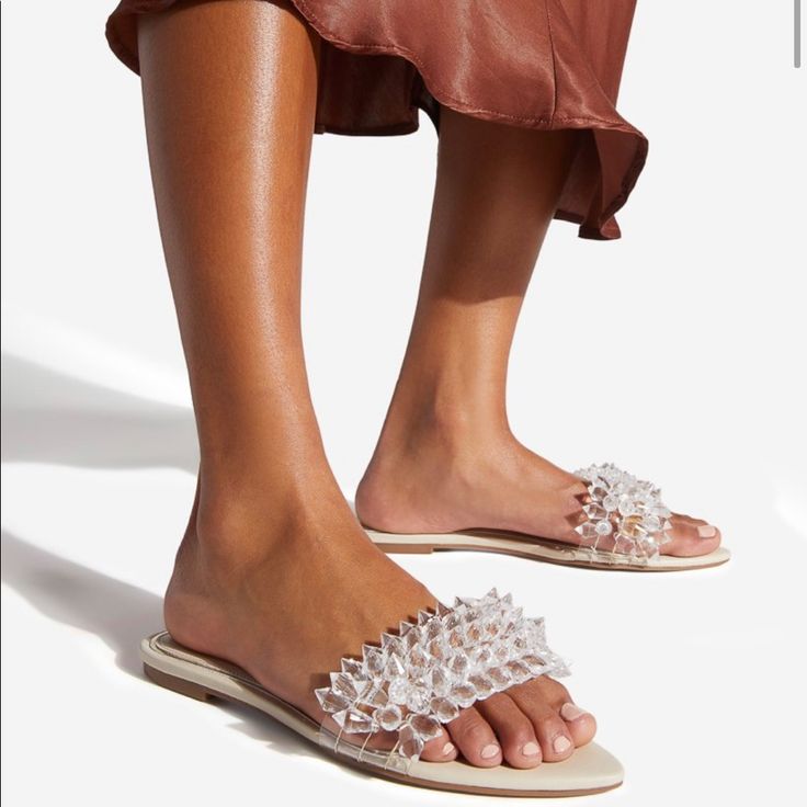 A Slip-On Flat Sandal With An Embellished Strap. Material: Faux-Leather Features: Extra Padding For Added Comfort Outside Heel Height: .25" Chic Beaded Open Toe Sandals, Embellished Synthetic Toe Post Sandals, Chic Embellished Sandals For Vacation, Beaded Open Toe Synthetic Sandals, Leather Sandals With Rhinestones And Flat Heel, Leather Flat Heel Sandals With Rhinestones, Beaded Synthetic Open Toe Sandals, Glamorous Slip-on Synthetic Sandals, Summer Beaded Synthetic Sandals