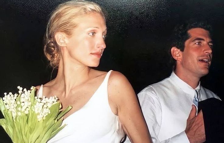 a man standing next to a woman in a white dress holding a bouquet of flowers