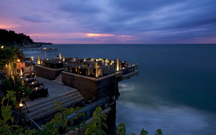 an outdoor dining area overlooking the ocean at dusk with candles lit up on the steps