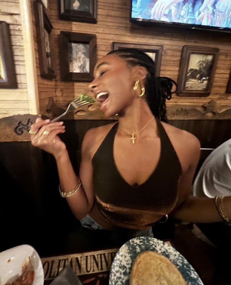 a woman sitting at a table with food in front of her and eating from a fork