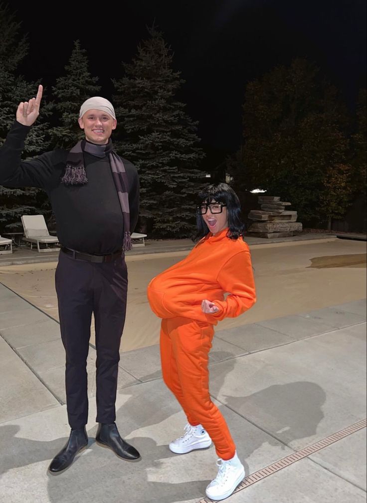 an older man and woman in orange outfits posing for a photo at night with trees in the background