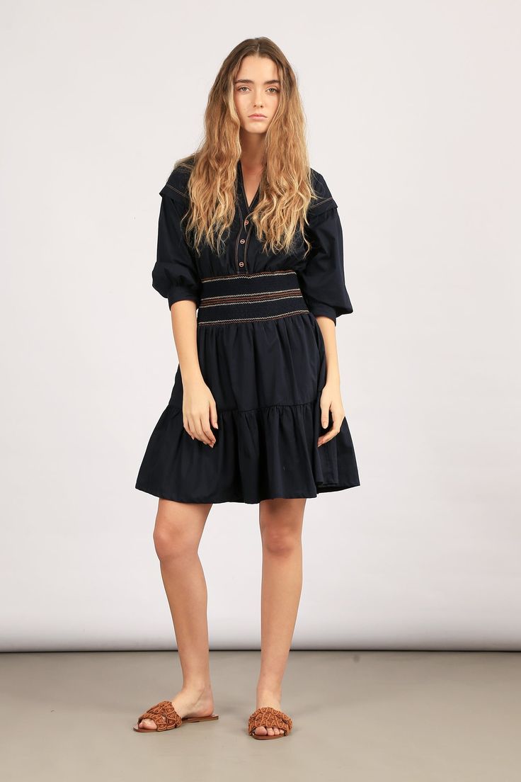 Elevate your style with our Mercy Dress – a blend of elegance and comfort. Crafted from 100% cotton, this mini dress is available in striking blue and classic black. The pleated ruffled skirt adds a playful touch, while the elasticated belt with contrasting stitching details defines your silhouette. Make a statement in our Mercy Dress! Size & Fit Fits true to size, take your normal size Designed to be worn loosely fitted Model is 5’10’’ (1.75 mt) and is wearing a size S Detalis & Care 100% cotton Mini dress Shirt collar V-neckline Buttons on chest to the waist Elasticated belt with stitching details in contrasting colours Long sleeves with detail on dropped shoulders Elasticized cuffs Pleated ruffled skirt Machine wash cold, do not bleach, tumbly dry gentle Daywear Mini Dress With Ruffled Skirt, Mini Dress With Ruffled Skirt For Daywear, Mini Length Ruffled Skirt Dress For Daywear, Chic Mini Dress With Pleated Hem For Daywear, Elegant Pleated Cotton Mini Dress, Navy Midi Dress With Ruffles, Navy Midi-length Dress With Ruffles, Navy Ruffled Midi Dress, Chic Cotton Tiered Dress With Ruffle Hem