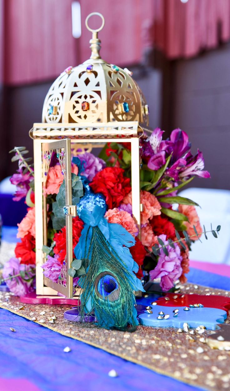 a table topped with a birdcage filled with flowers next to a blue cloth covered table