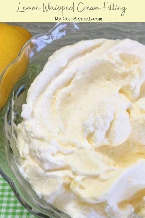 a glass bowl filled with whipped cream next to an orange on a green checkered tablecloth