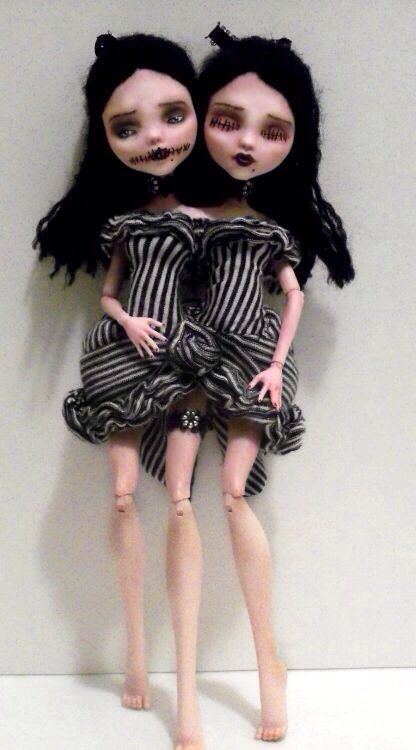 two creepy dolls sitting next to each other on a white surface in front of a wall