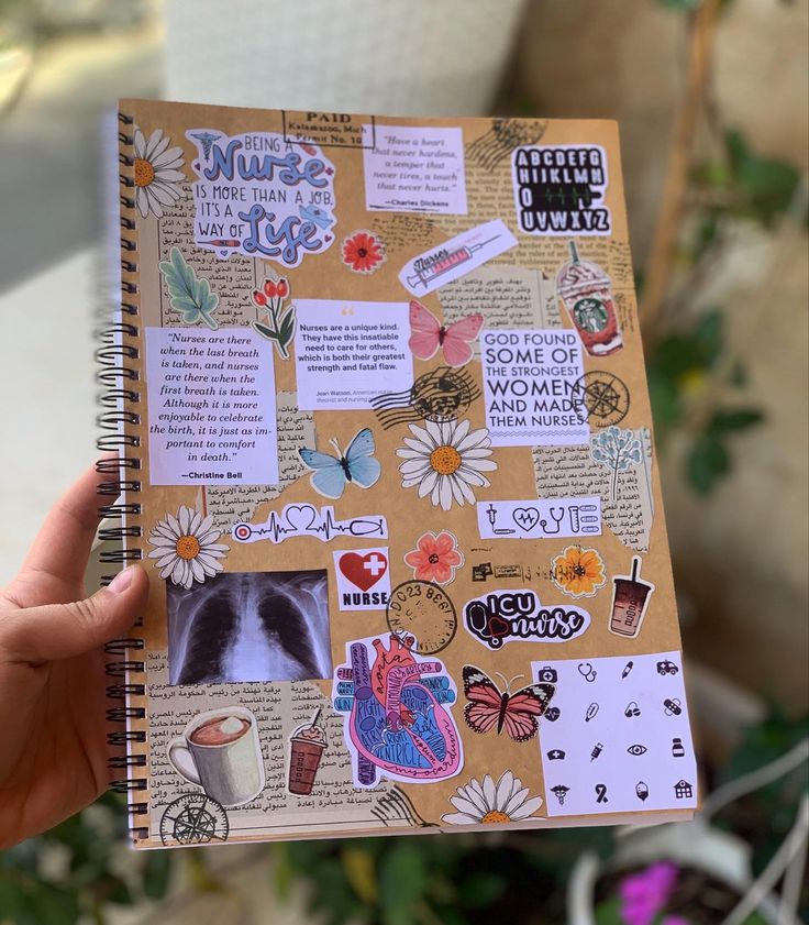 a person holding up a book with stickers and pictures on the pages, in front of a potted plant