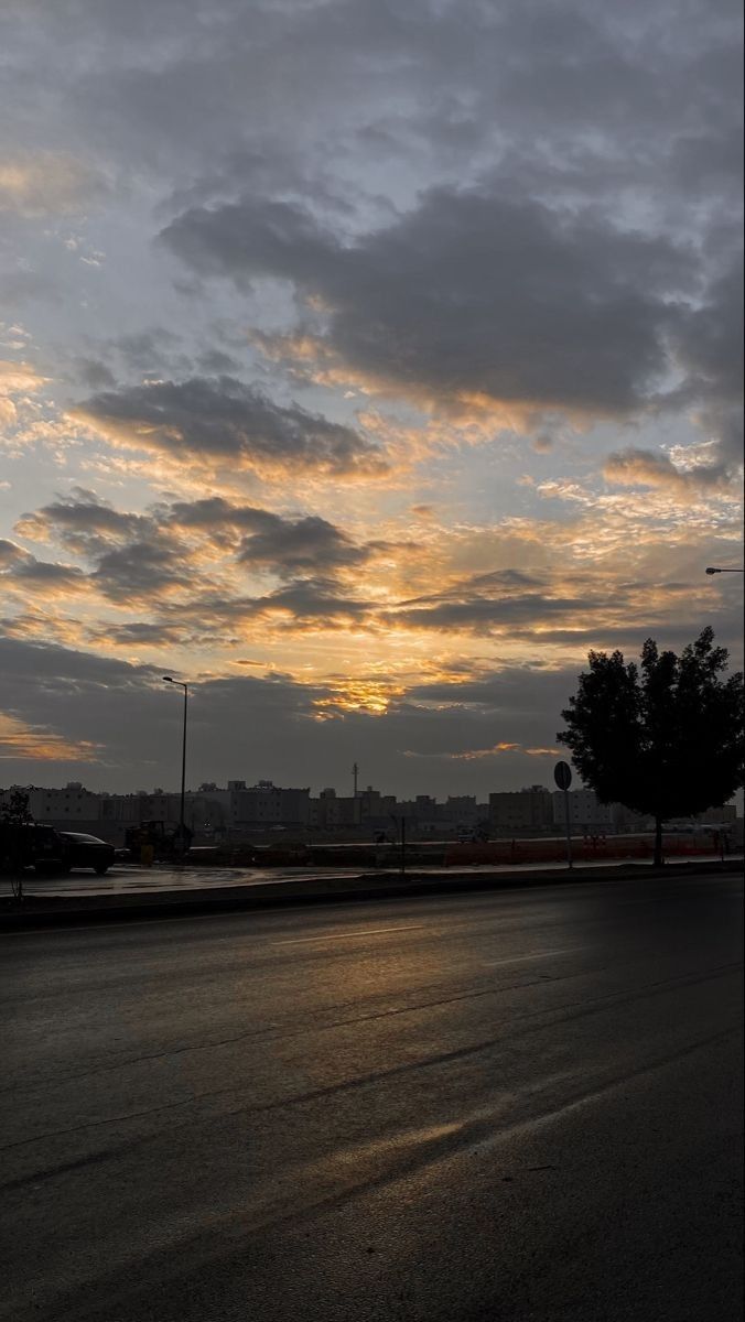 the sun is setting behind some clouds in the sky over an empty street with no cars on it