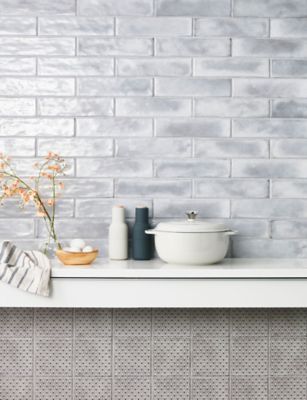 a white counter top sitting next to a bowl and vase with flowers on it in front of a brick wall