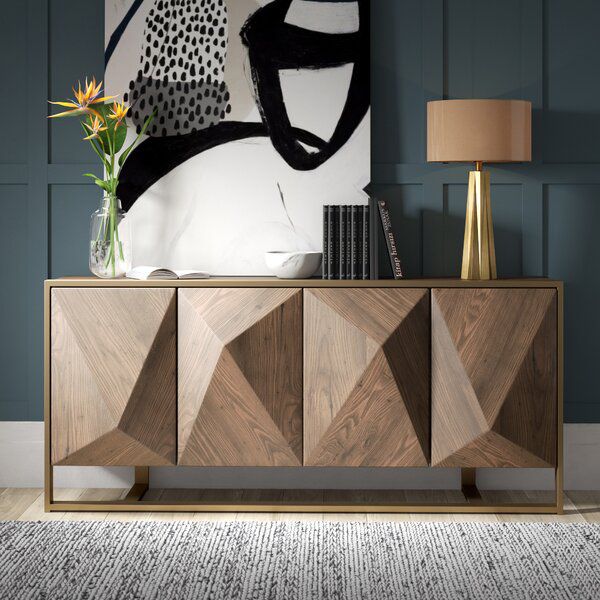 a sideboard with an abstract painting on the wall behind it and a lamp next to it