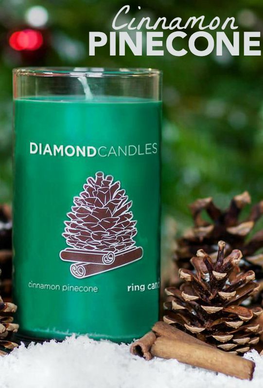 a green candle sitting on top of snow next to pine cones and christmas decorations with the words cinnamon pinecone