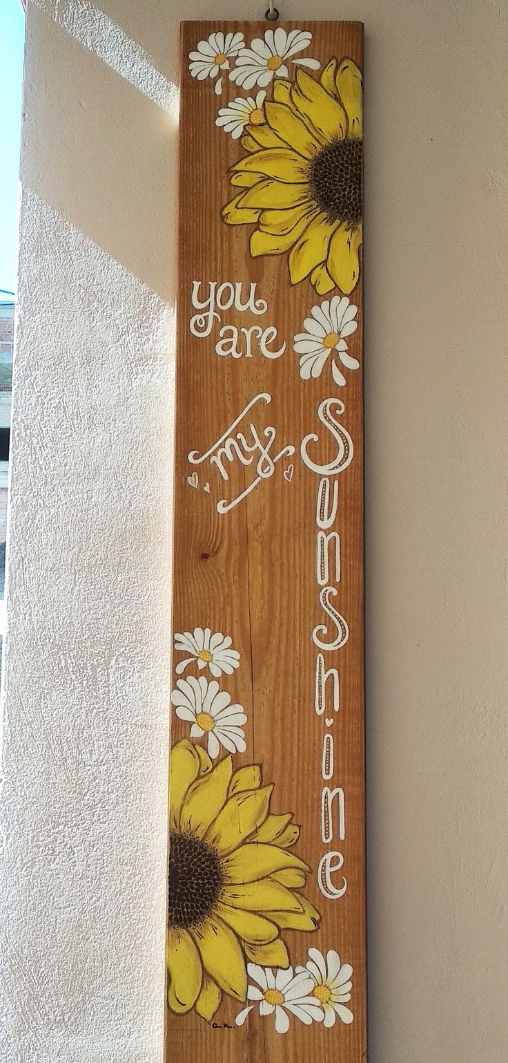 a wooden sign hanging on the side of a building with sunflowers painted on it