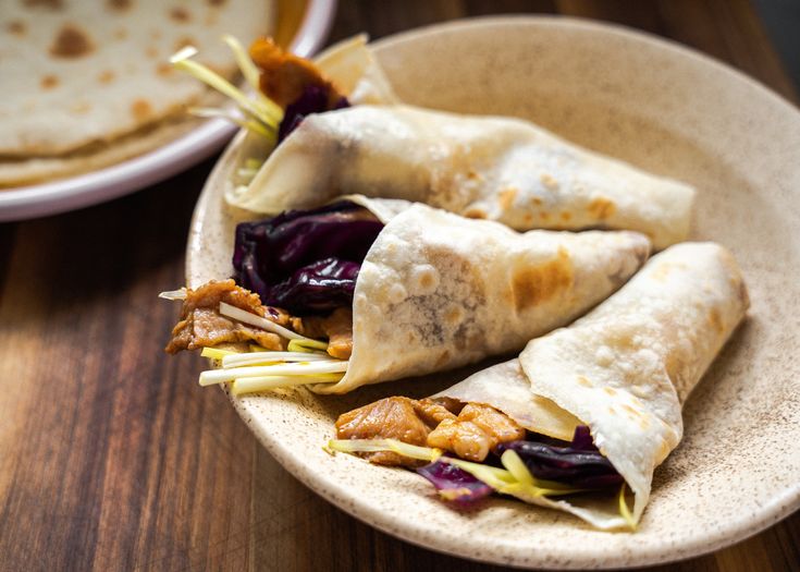 two burritos with meat and vegetables on a plate next to a tortilla