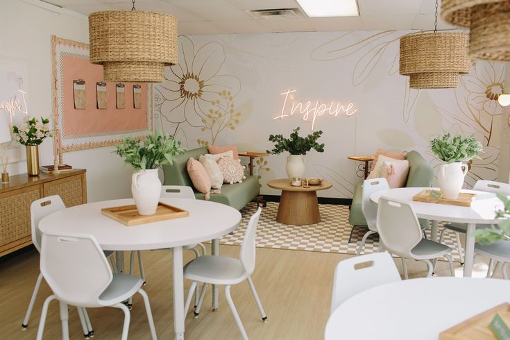 a room with white tables and chairs, plants on the wall and pink flowers in baskets hanging from the ceiling