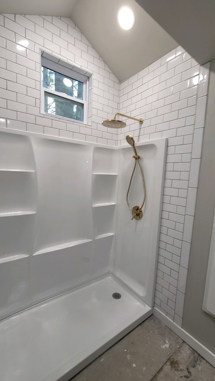 a bathroom with white tile walls and flooring, including a shower head in the corner