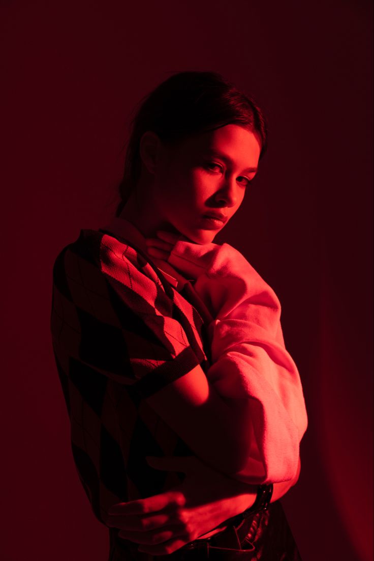 a woman standing in the dark with her arms folded over her chest and looking down