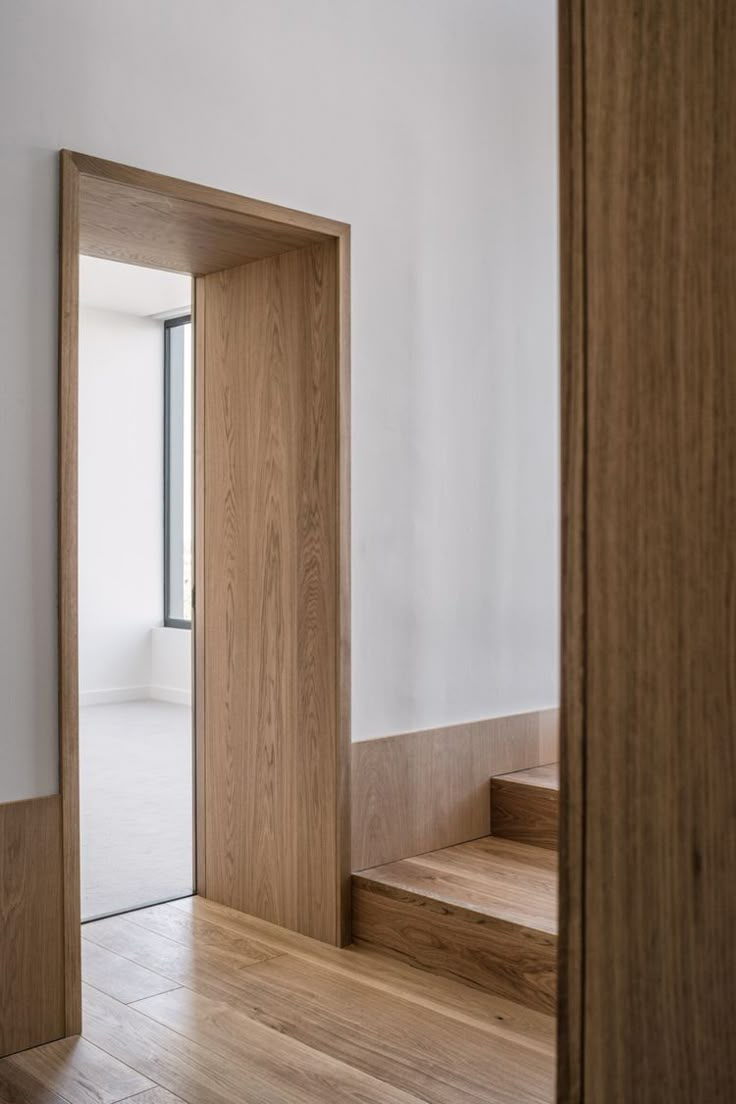 an open door leading to a white room with wooden floors and stairs in the background