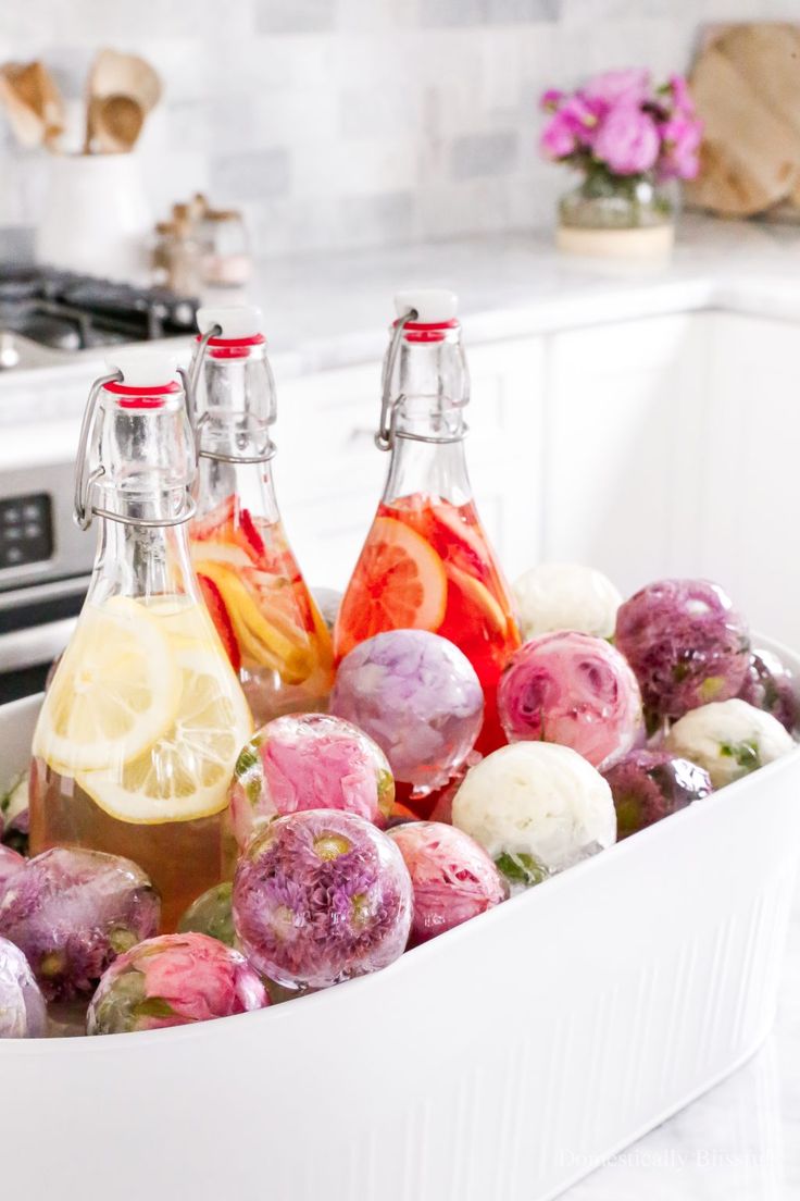 three bottles of lemonade and some fruit in a white container on a counter top