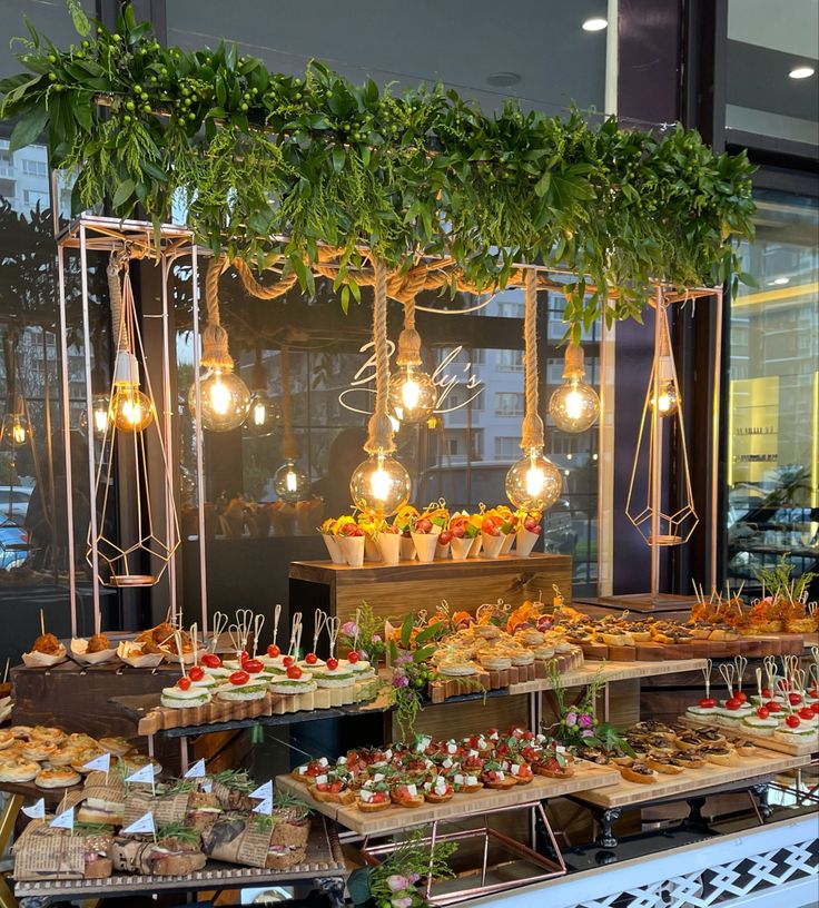 an assortment of desserts on display in a store window with lights hanging from the ceiling