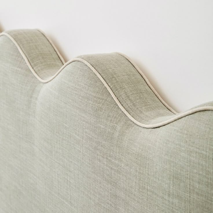 the back end of a couch that is upholstered with beige fabric and white piping