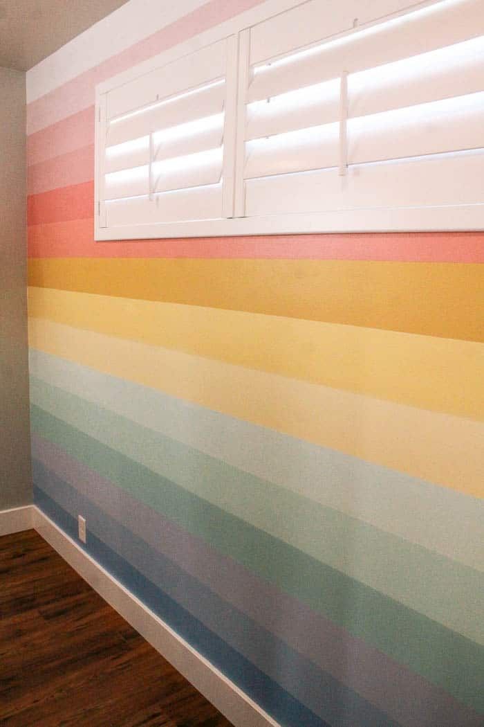 an empty room painted with multicolored stripes on the wall and window shutters