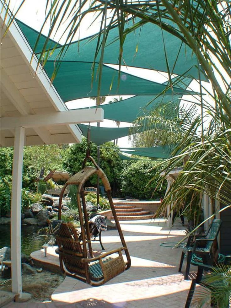 a swing chair sitting on top of a patio next to a lush green umbrella covered area