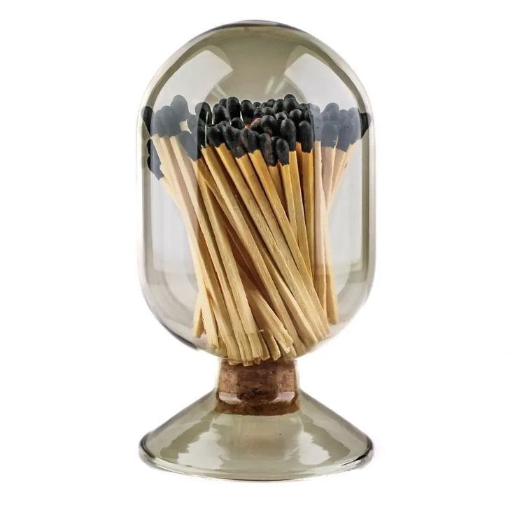 a glass jar filled with matches on top of a wooden stick holder in front of a white background