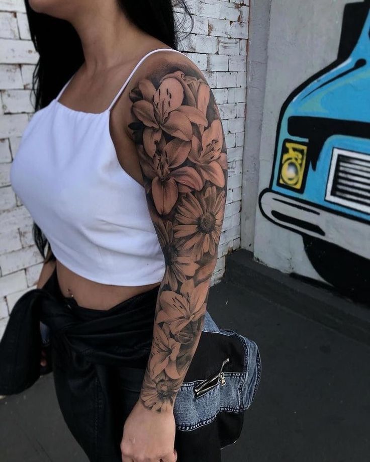 a woman with a flower tattoo on her arm is walking down the street in front of a brick wall