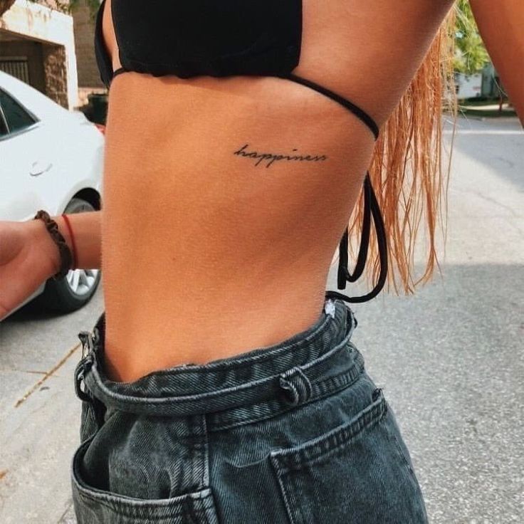 a woman with a tattoo on her lower back and the word happiness written in cursive writing