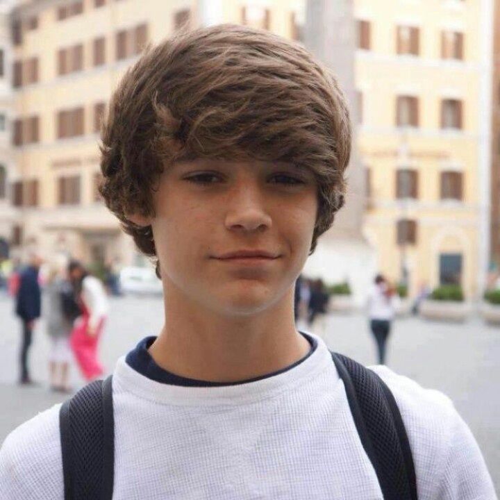 a young man is standing in front of some buildings and looking at the camera with a serious look on his face