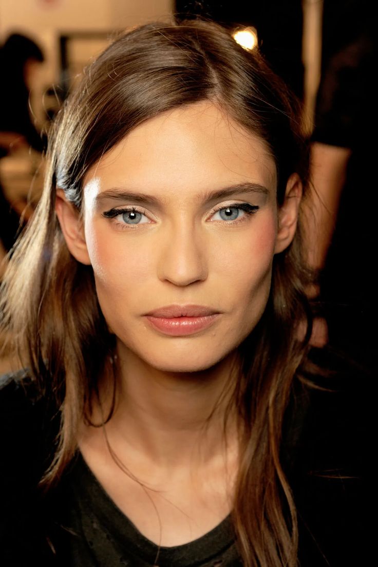 a woman with long hair and blue eyes is looking at the camera while she's getting her make - up done