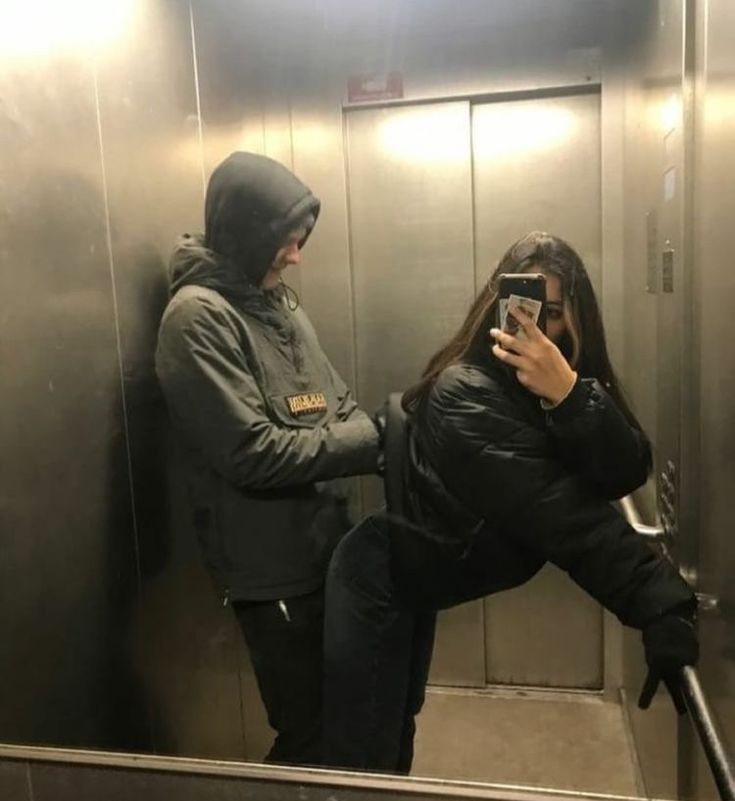 a woman taking a selfie in an elevator while another person takes a picture with their cell phone