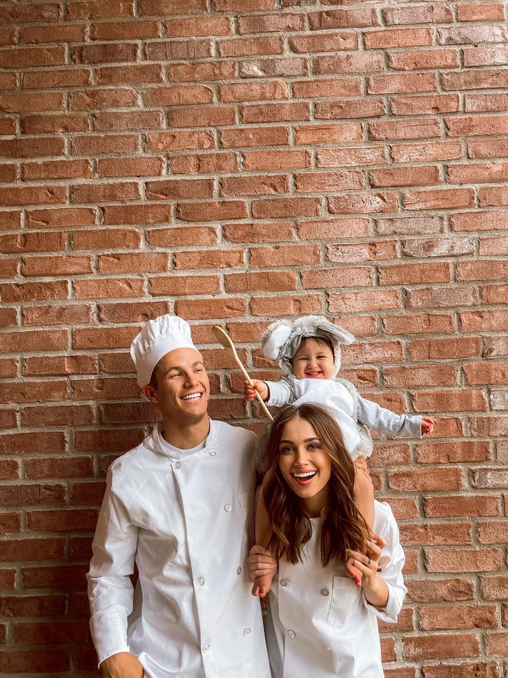 a man, woman and child dressed up in chef's uniforms standing next to a brick wall