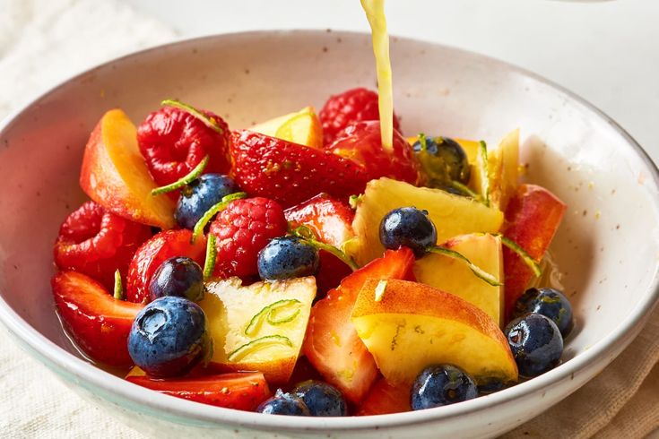 fresh fruit salad with oranges, strawberries and blueberries being poured into a bowl