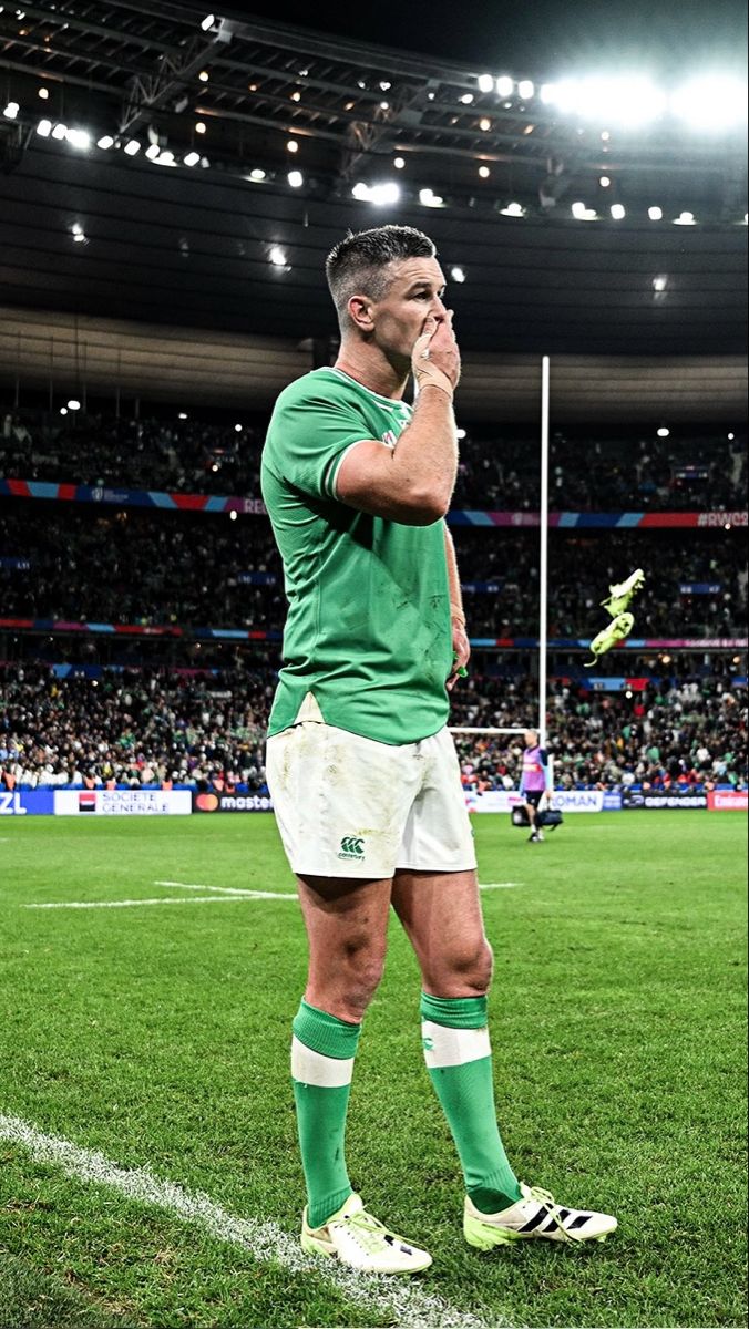 a rugby player is standing on the field with his hand in his mouth and looking down