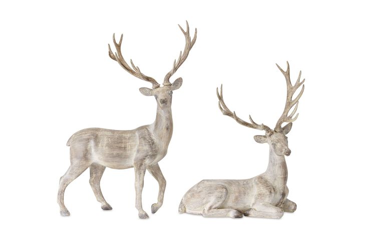 two deer figurines sitting next to each other on a white surface with one standing and the other laying down