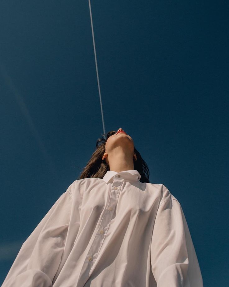 a woman flying a kite high in the sky with her head tilted to the side