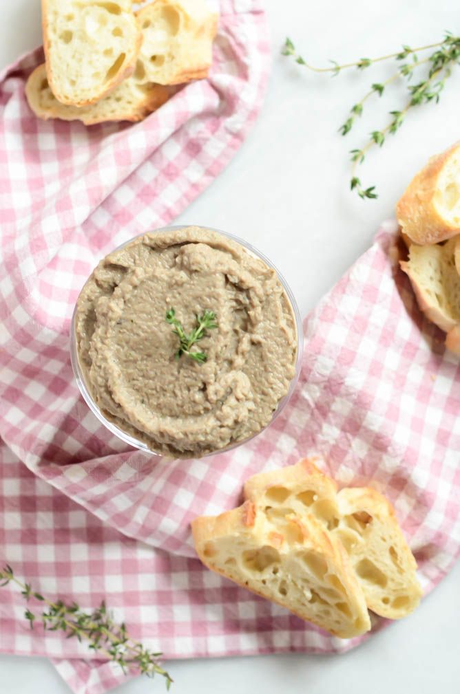 a small bowl of hummus on a pink and white checkered cloth next to two slices of bread