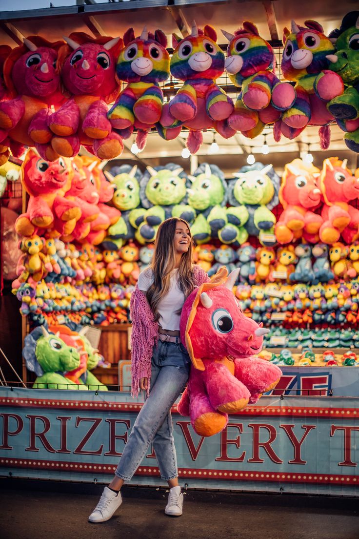 a woman holding a pink stuffed animal in front of a carnival