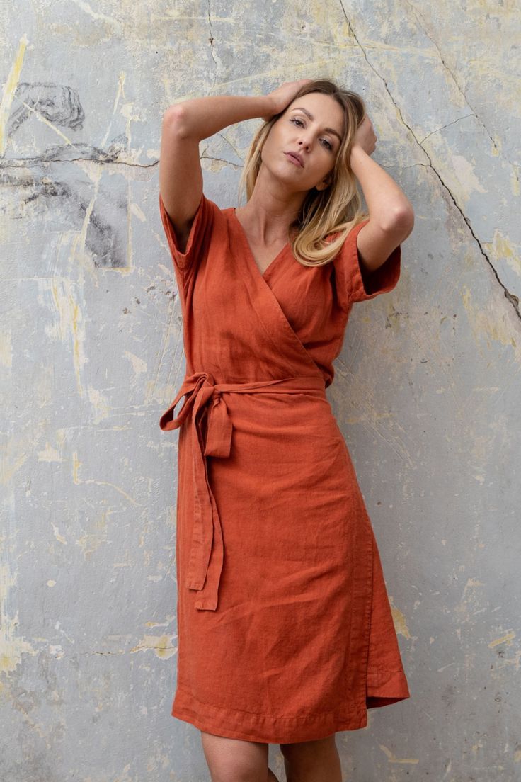 Woman posing with a cinamon red color linen dress ELIANA Casual Wrap Dress With Surplice Neckline For Beach, Summer Wrap Dress With Tie Waist And Surplice Neckline, Summer Vacation Wrap Dress With Surplice Neckline, Summer V-neck Wrap Dress For The Beach, Summer V-neck Wrap Dress For Beach, Summer Wrap Dress With Surplice Neckline For Beach, Fitted Wrap Dress With Tie Waist For Beach, Fitted Tie Waist Wrap Dress For The Beach, Summer Wrap Dress With Tie Waist For Vacation